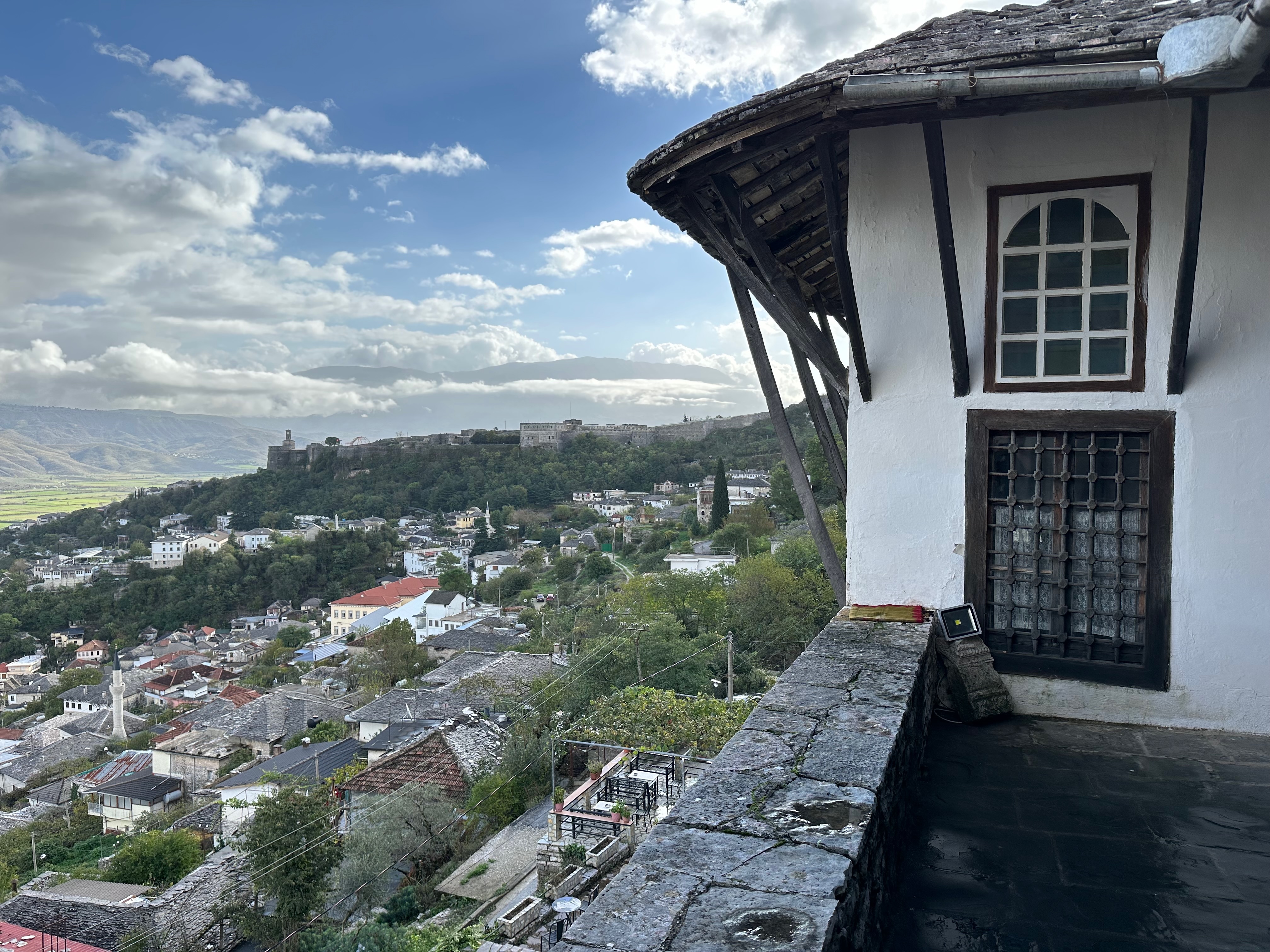 Gjirokastër Fortress above layered stone-roofed Ottoman houses on the historic hillside, with the Drino Valley mountains beyond in Albania