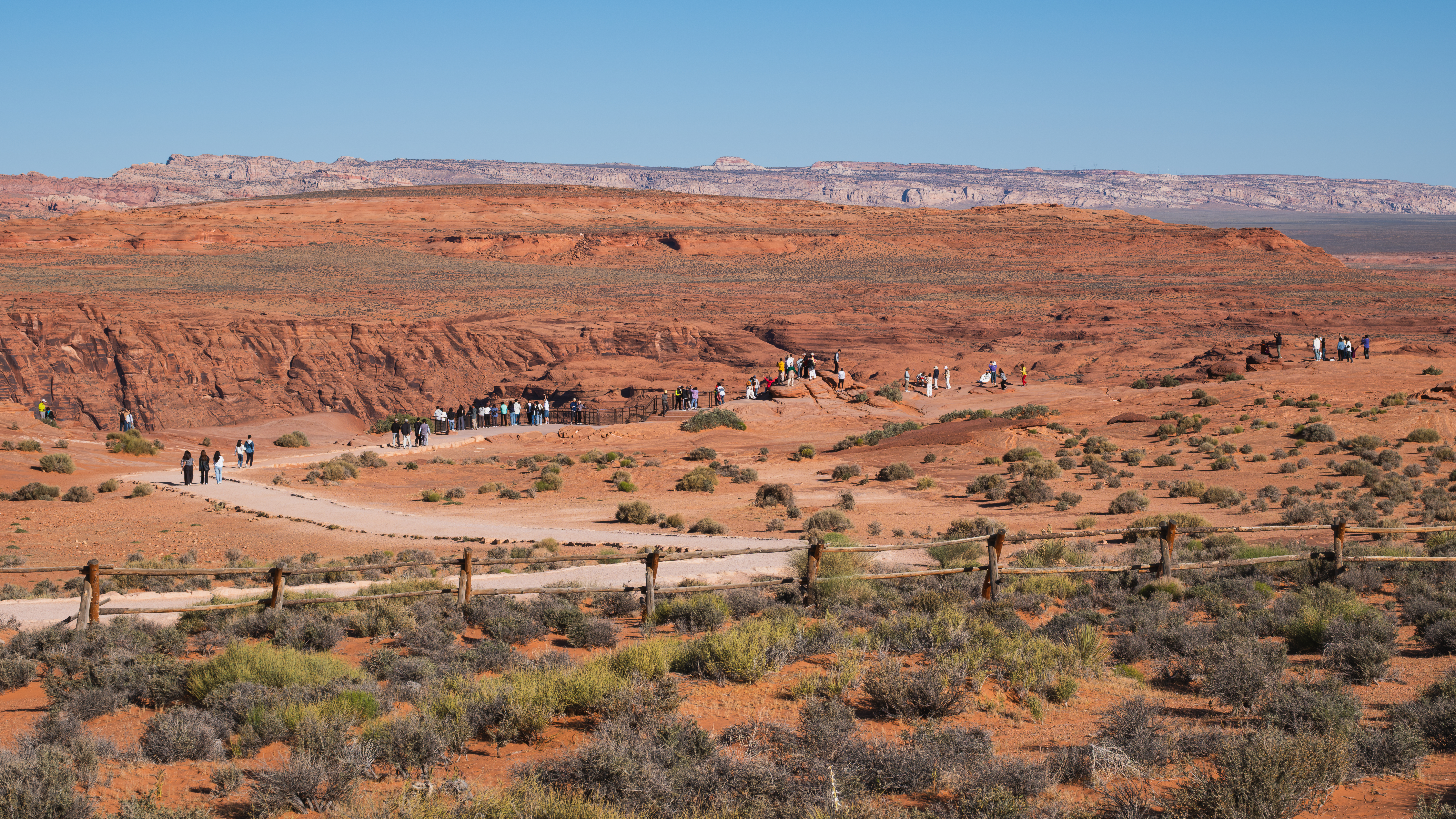 Travelers gathering at the broad sandstone overlook above Horseshoe Bend