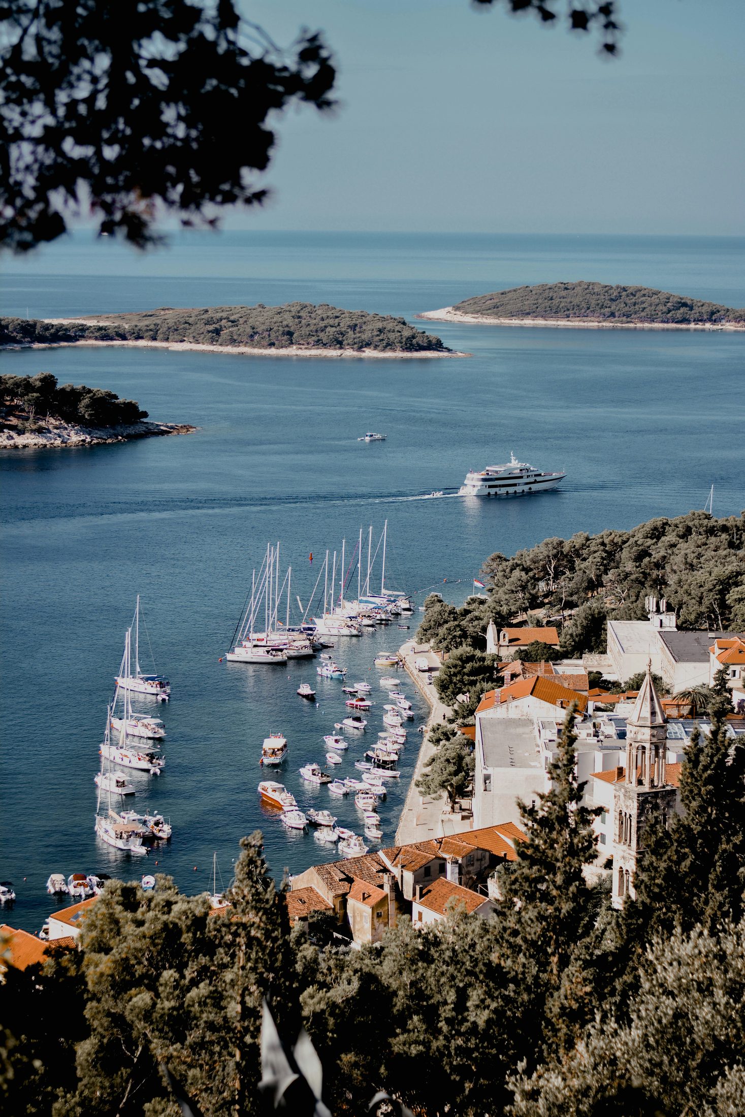 A small coastal ship and sailboats in Hvar Town harbor with the Pakleni Islands beyond