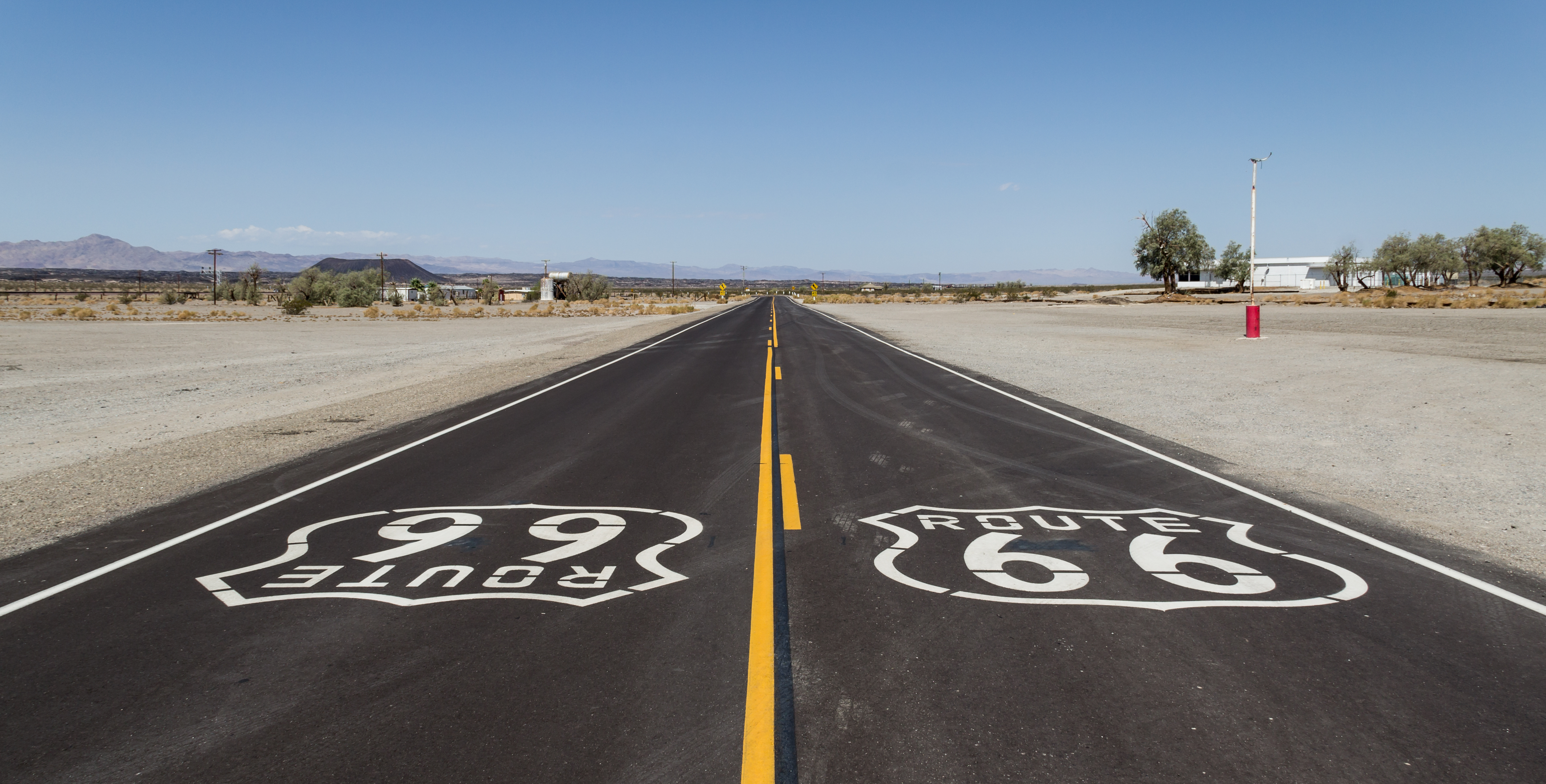 Two Route 66 pavement shields point in opposite directions on a long desert highway