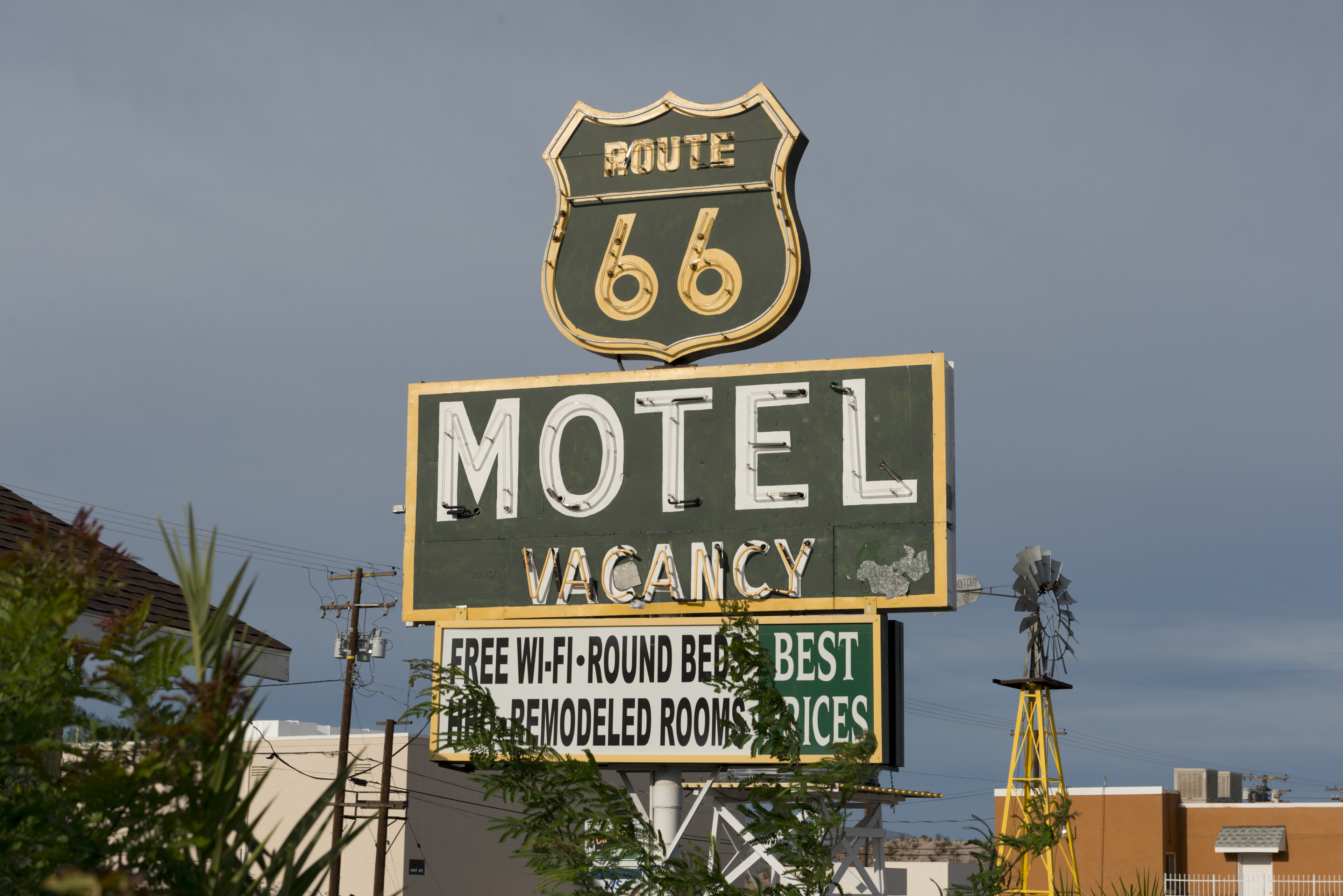 A working Route 66 motel vacancy sign rises above modern Barstow buildings and desert utility lines