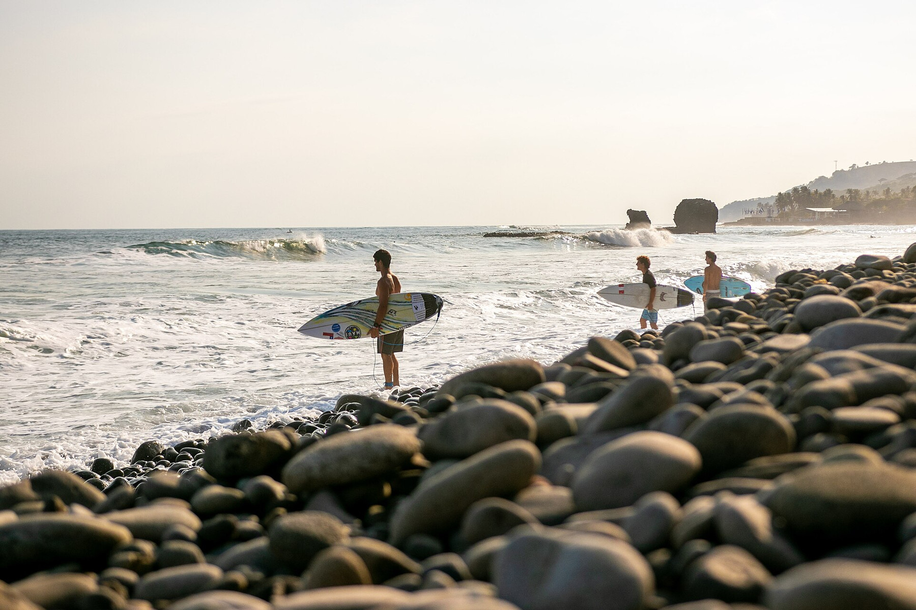 Surfers carrying boards across the black-stone beach at El Tunco, El Salvador