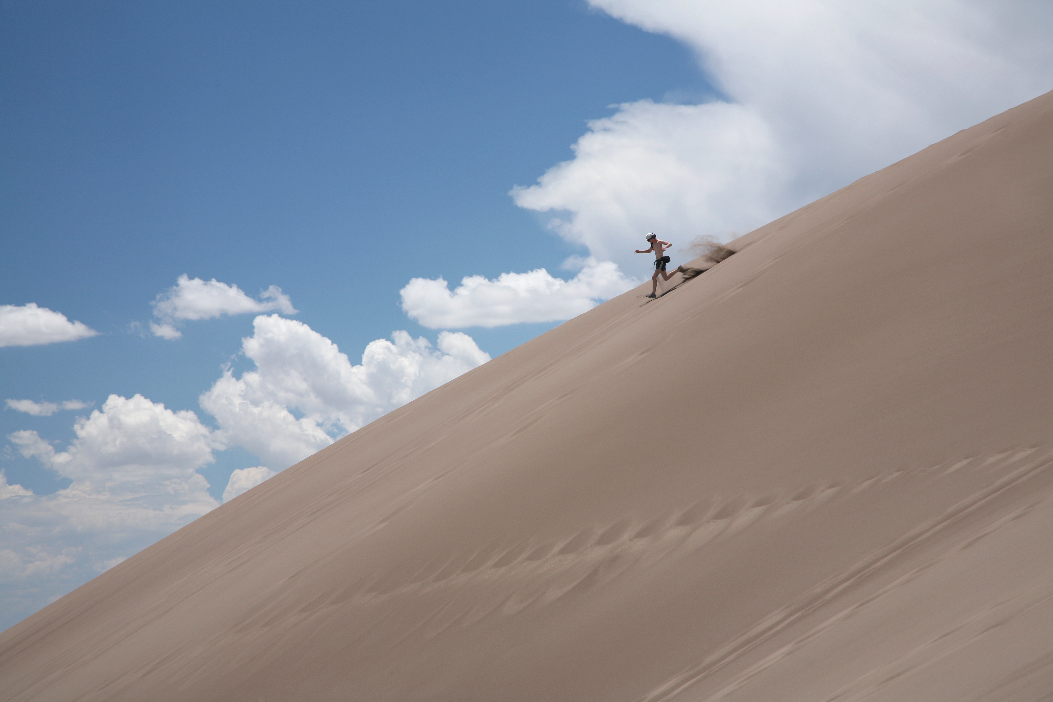 A visitor running down the immense diagonal face of a dune in Great Sand Dunes National Park