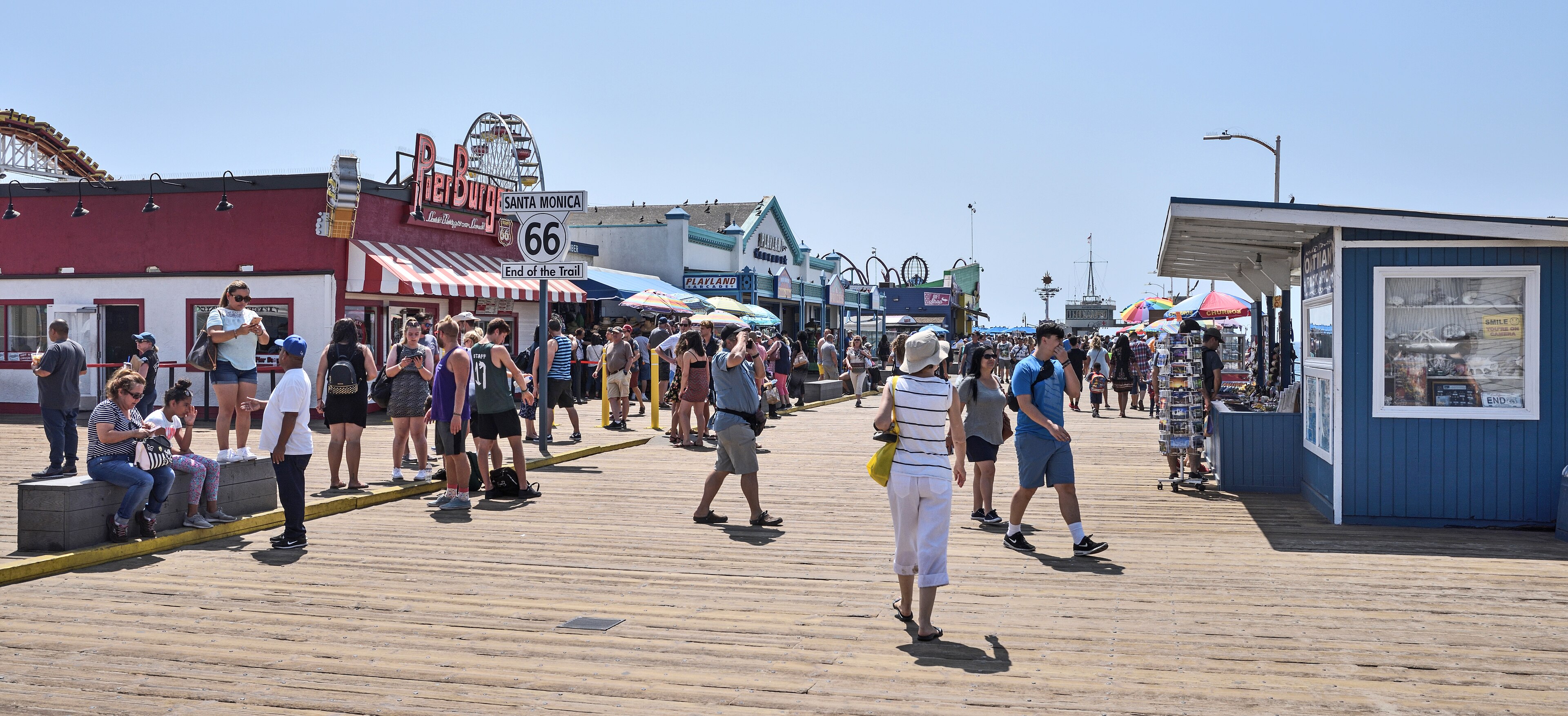 Travelers gather around the Route 66 End of the Trail sign on the busy Santa Monica Pier