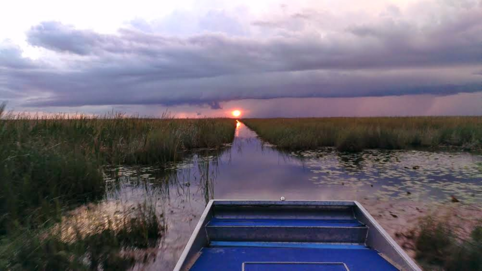 An airboat entering a sawgrass water trail beneath a dramatic Everglades sunset