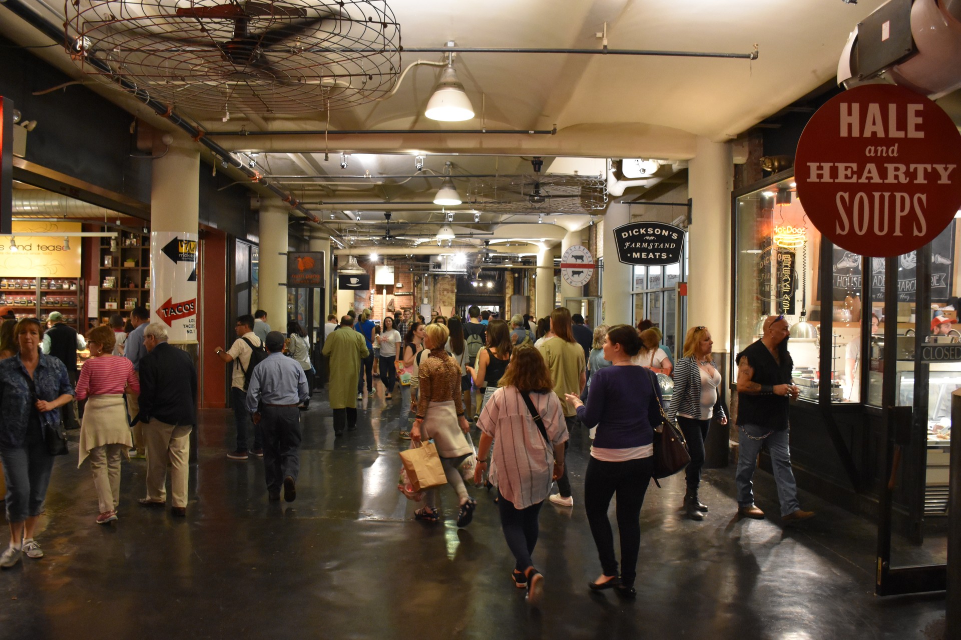 Crowds browse Chelsea Market food stalls beneath signs for tacos, soups, and a neighborhood butcher