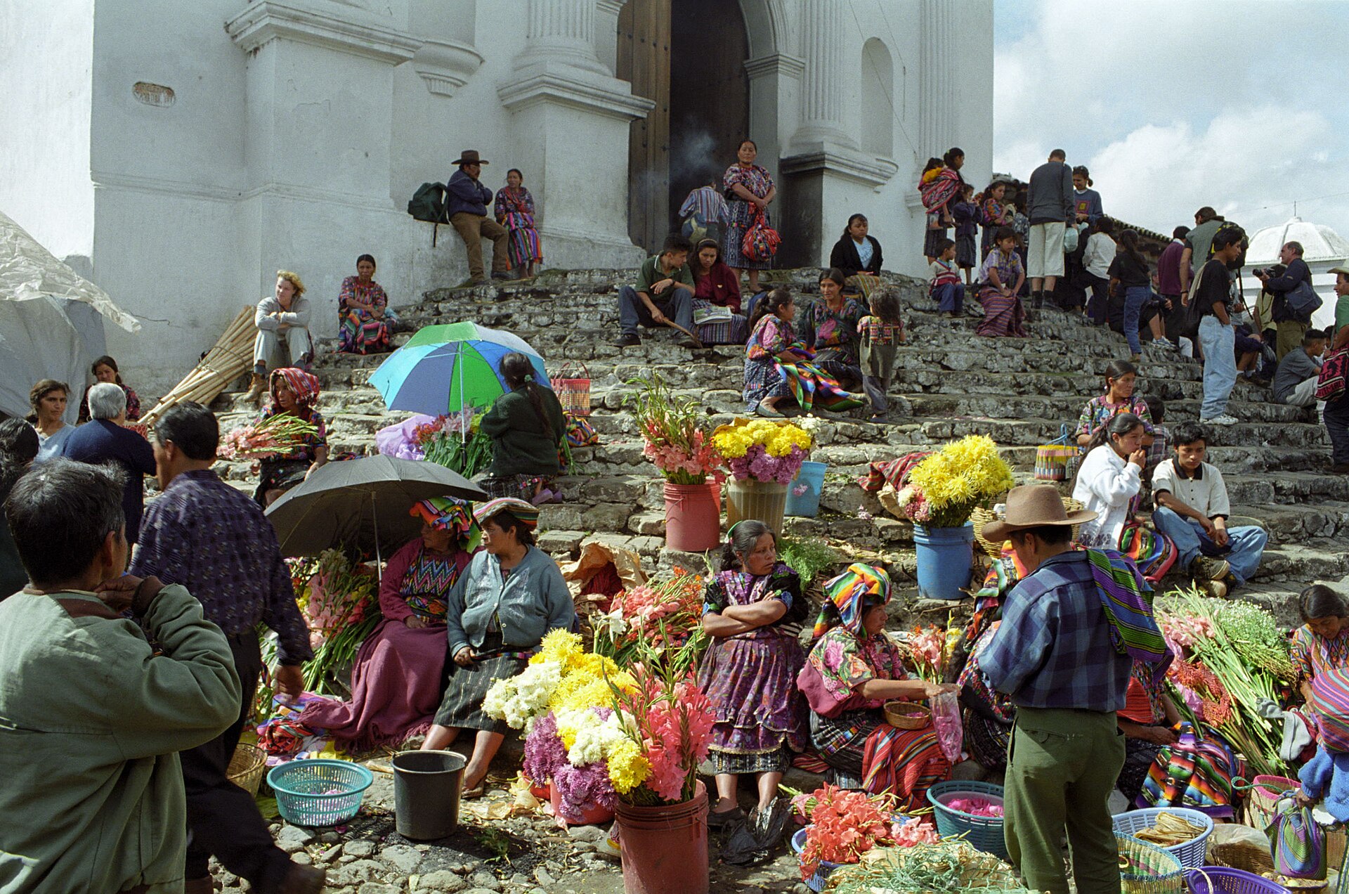 Vendors, shoppers, flowers, and woven clothing at the market on the steps of Santo Tomás Church in Chichicastenango, Guatemala