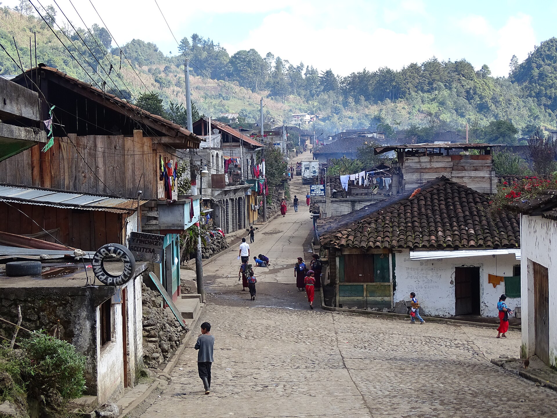 Residents walking through the cobbled Maya highland town of Chajul, Guatemala, with tiled village homes and cultivated mountain slopes