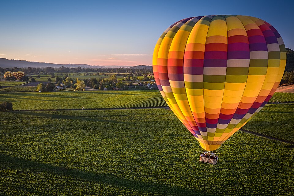 A hot-air balloon floating above the vineyard rows and hills of Napa Valley