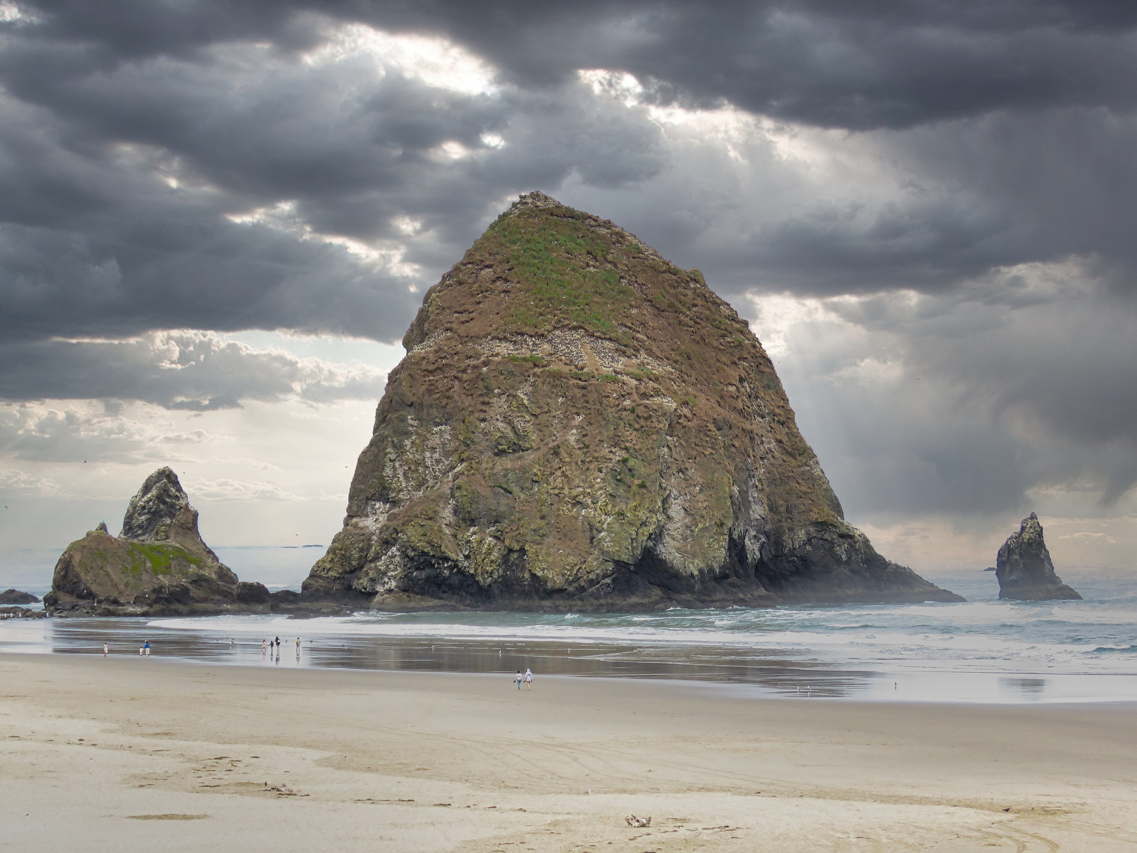 Visitors walking Cannon Beach beneath unmistakable Haystack Rock on the Oregon Coast