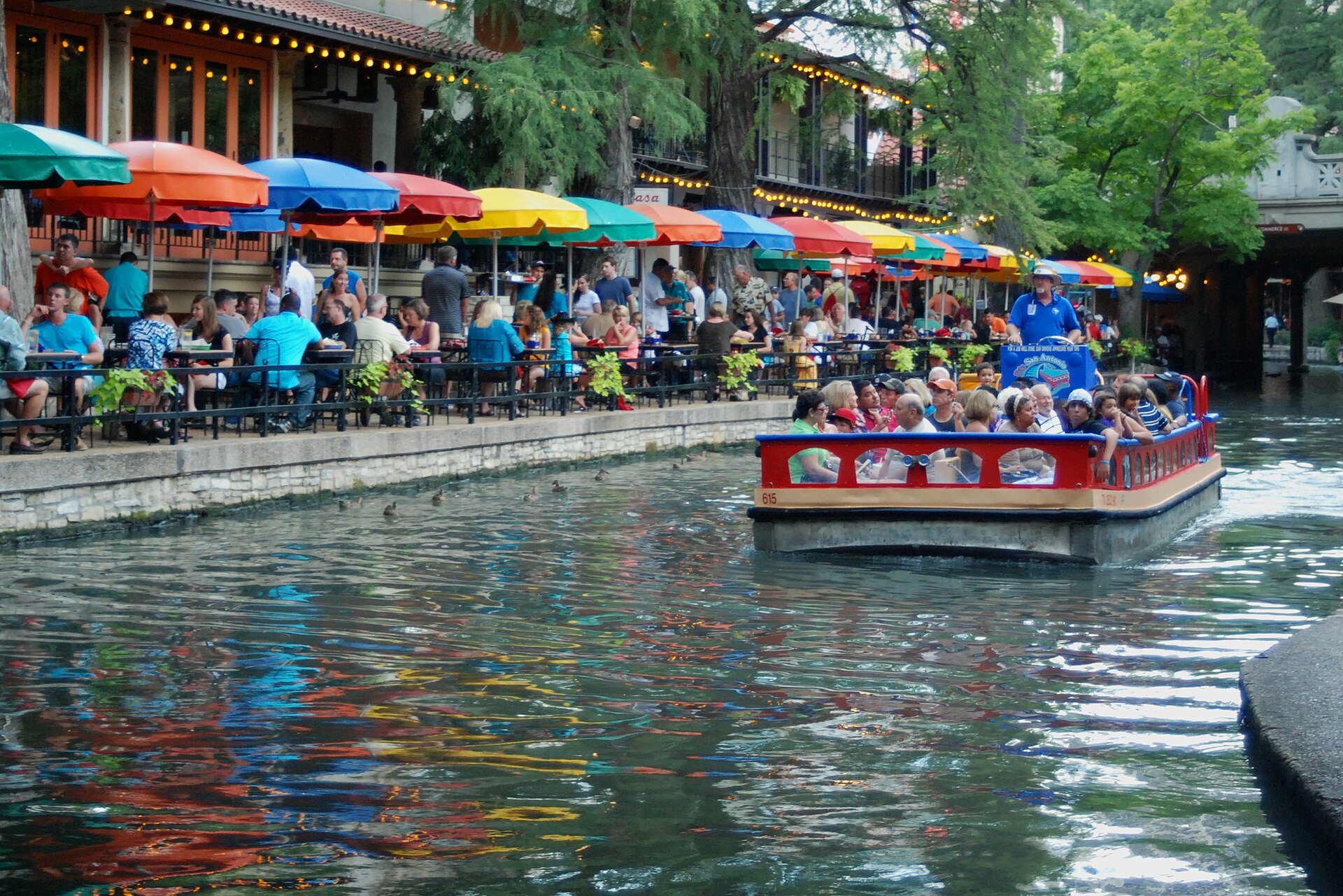Visitors, tour boats, restaurants, and colorful umbrellas along the San Antonio River Walk