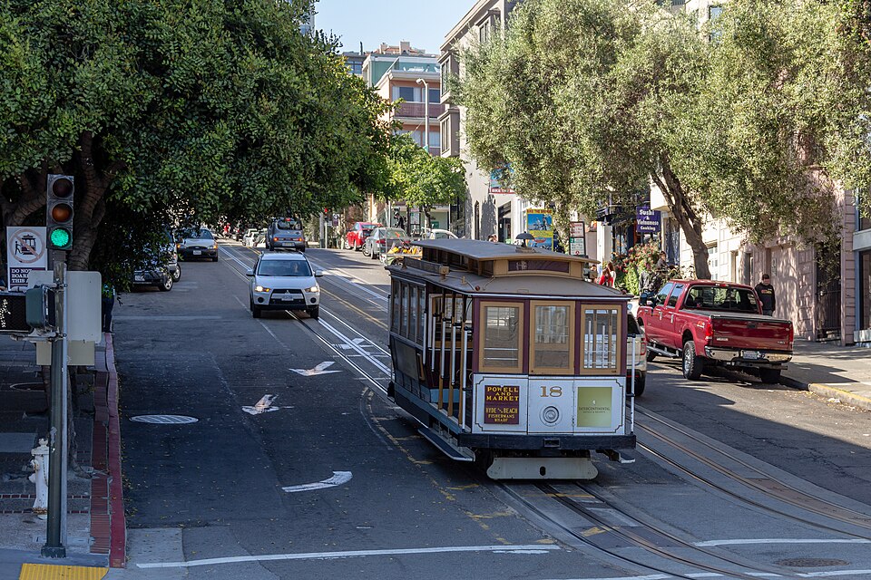 A San Francisco cable car climbing a neighborhood street between distinctive city buildings