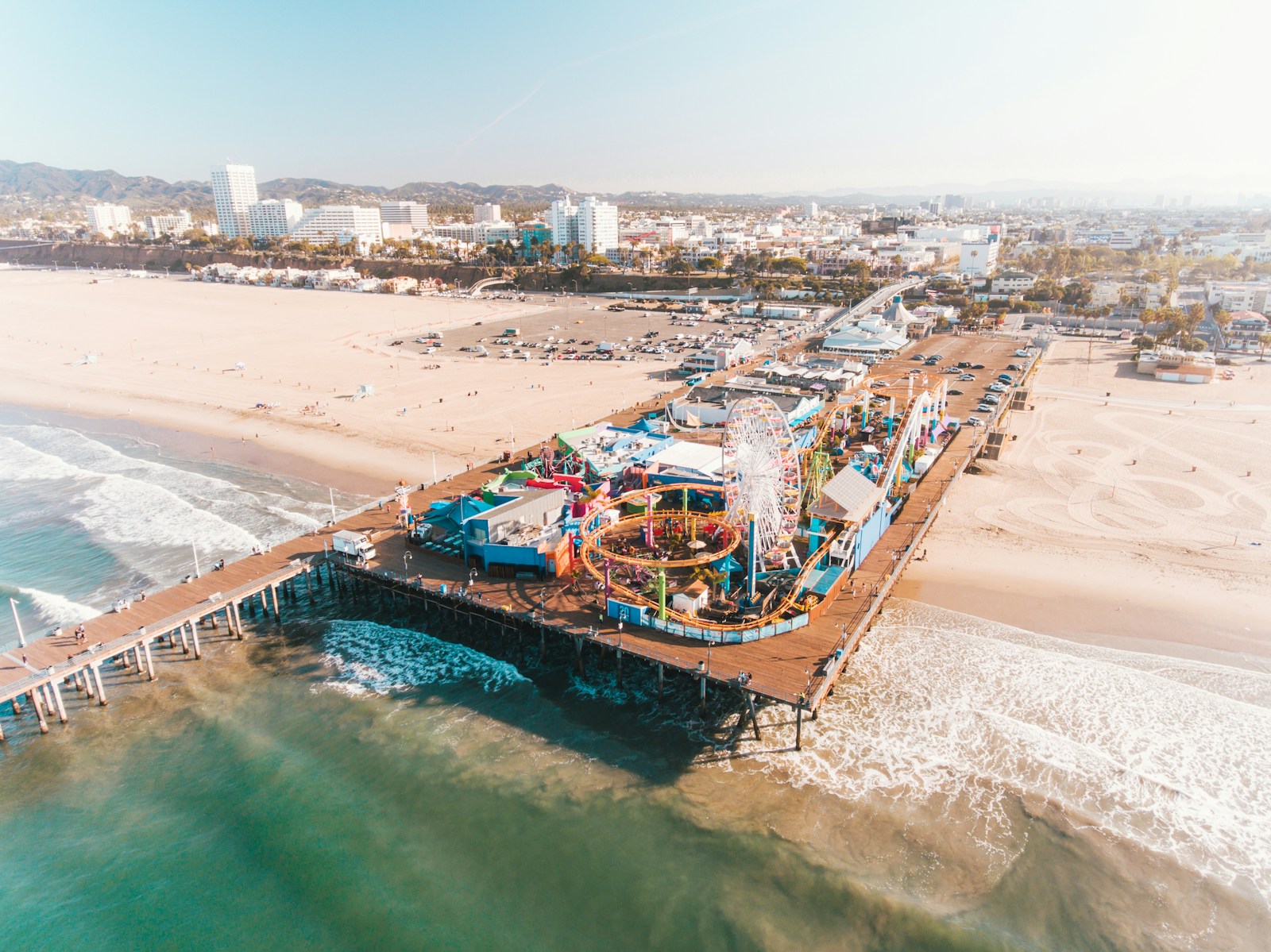 Santa Monica Pier extending into the Pacific beside a broad beach, coastal city, palms, and the Santa Monica Mountains