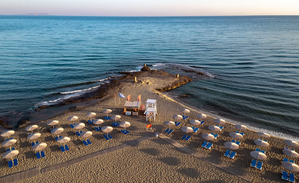 Lounge chairs and straw umbrellas arranged along a beach in Crete, Greece