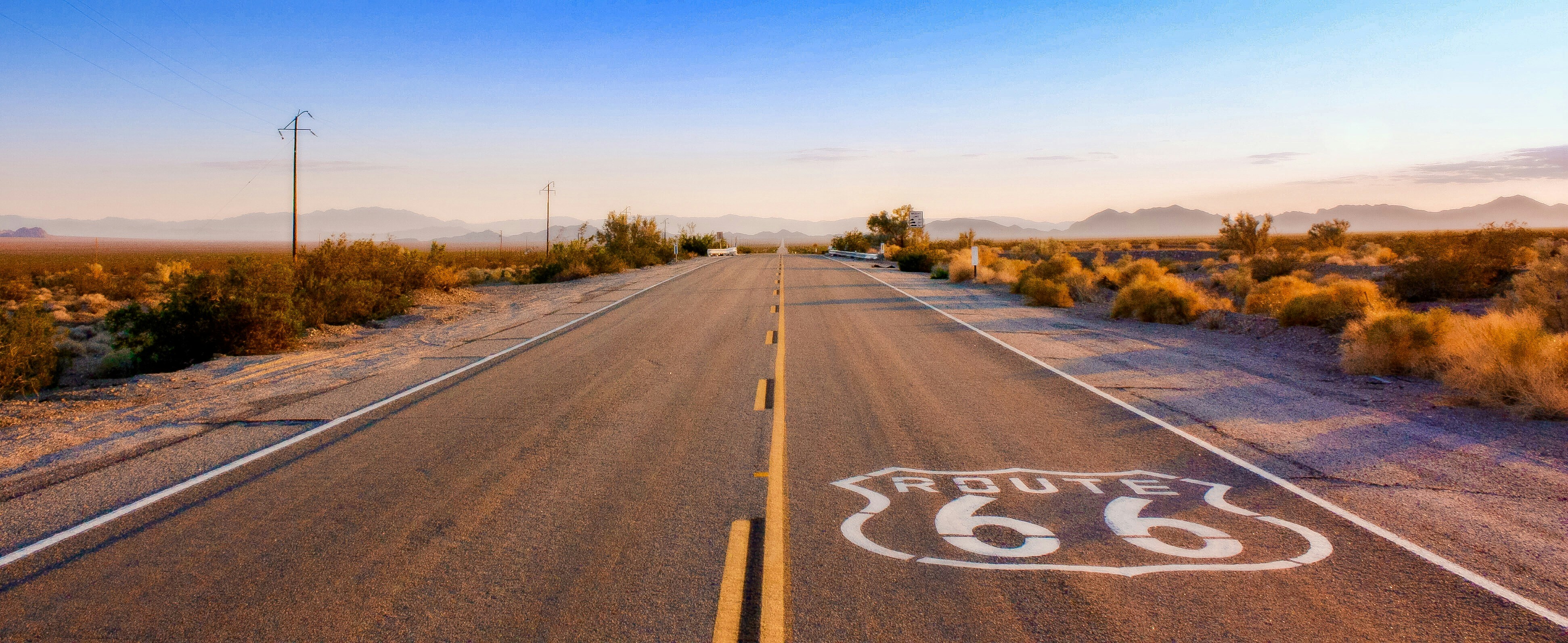 Historic Route 66 stretches toward distant desert mountains beneath a broad western sky