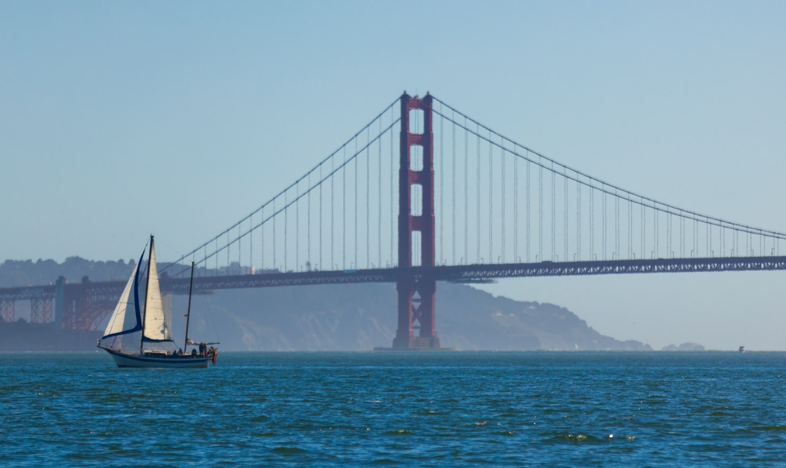 A sailboat passing beneath the Golden Gate Bridge in late California light