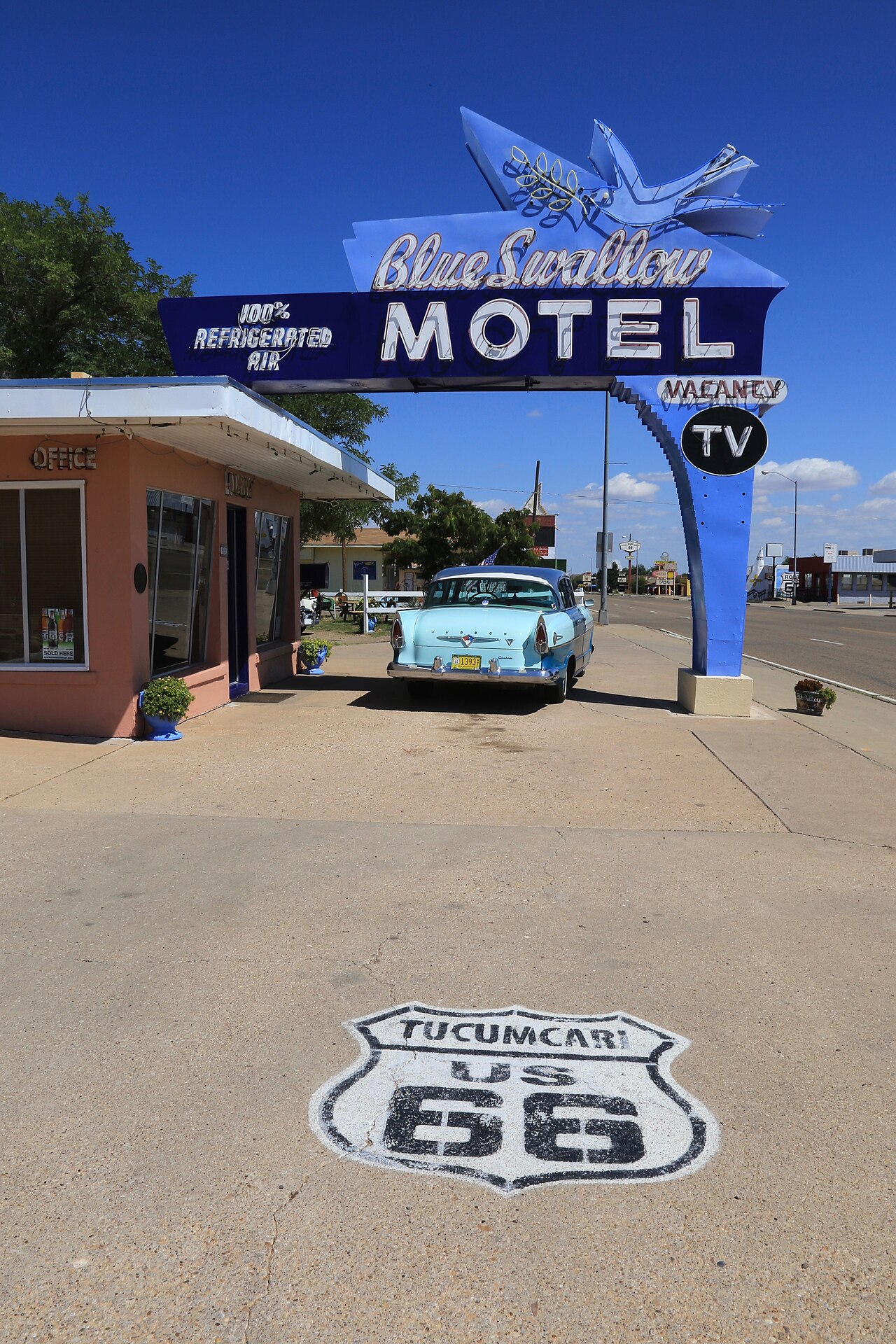 The Blue Swallow Motel sign, classic car, and Route 66 pavement shield mark Tucumcari's historic motor-court culture