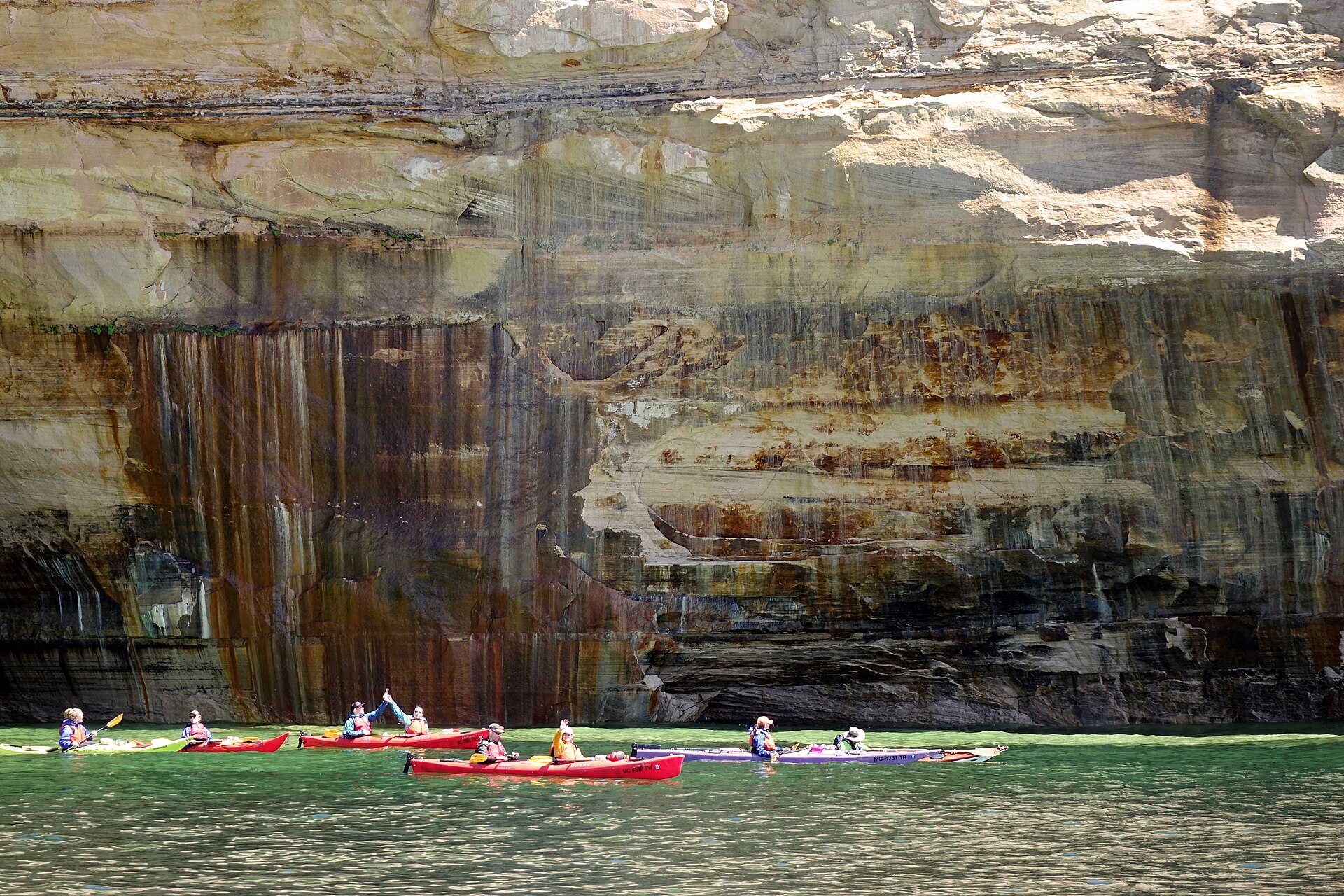 Kayakers paddle beneath the colorful sandstone cliffs of Pictured Rocks on Lake Superior