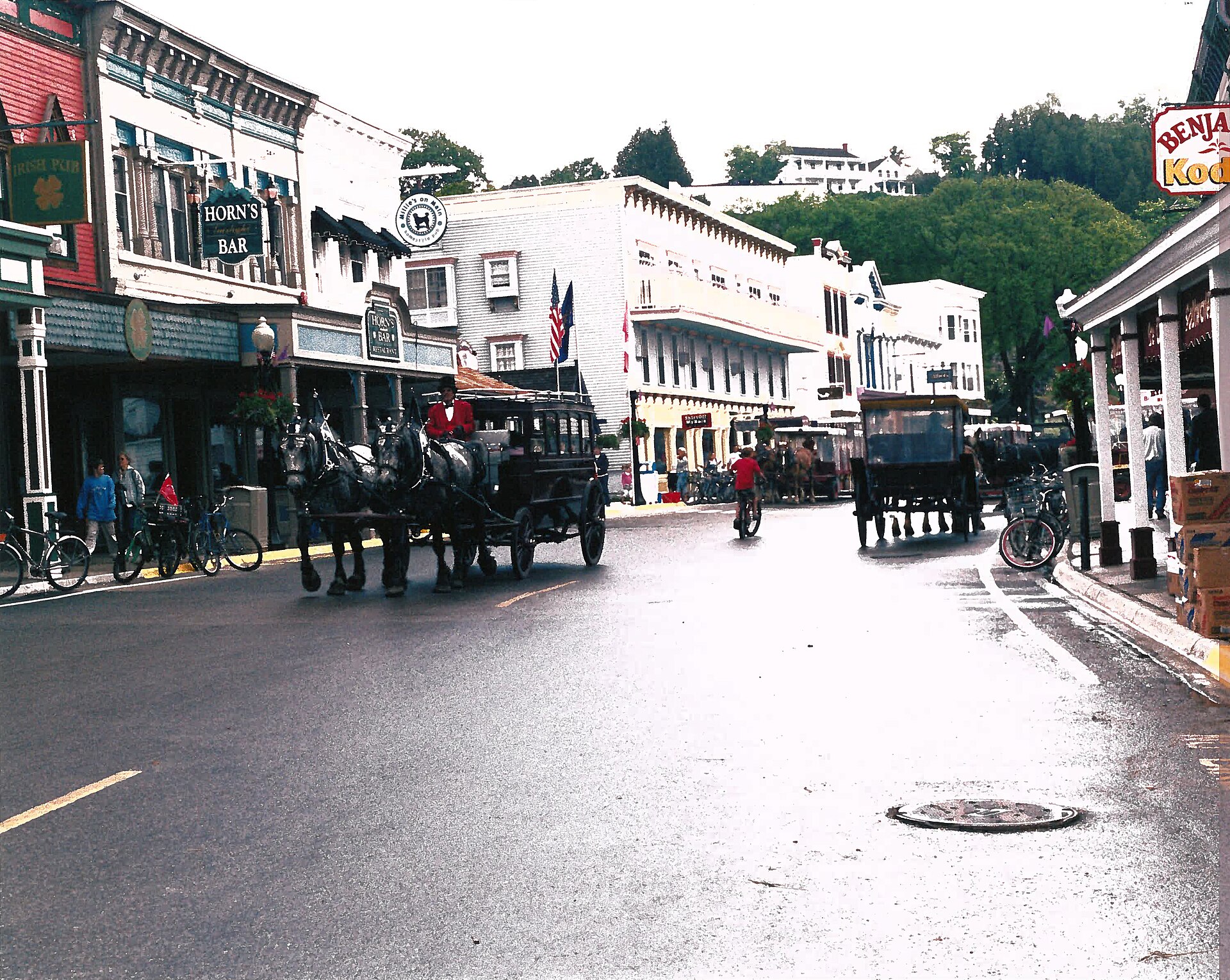 Horse-drawn carriages, bicycles, shops, and the Grand Hotel hillside animate Mackinac Island's Main Street