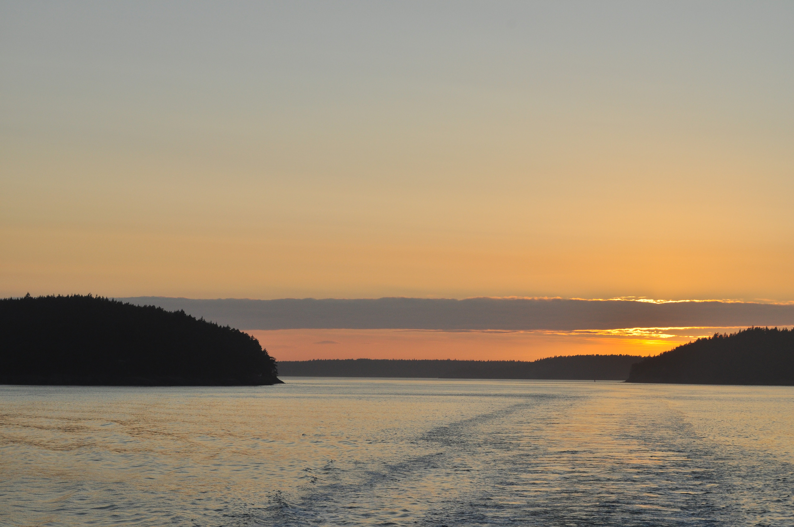 Sunset light stretching across water and forested islands in the San Juan archipelago