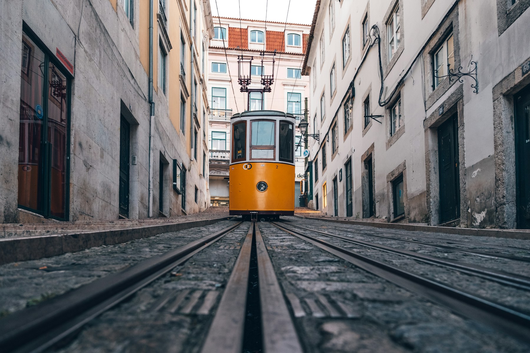 A yellow tram climbing a narrow Lisbon street in Portugal