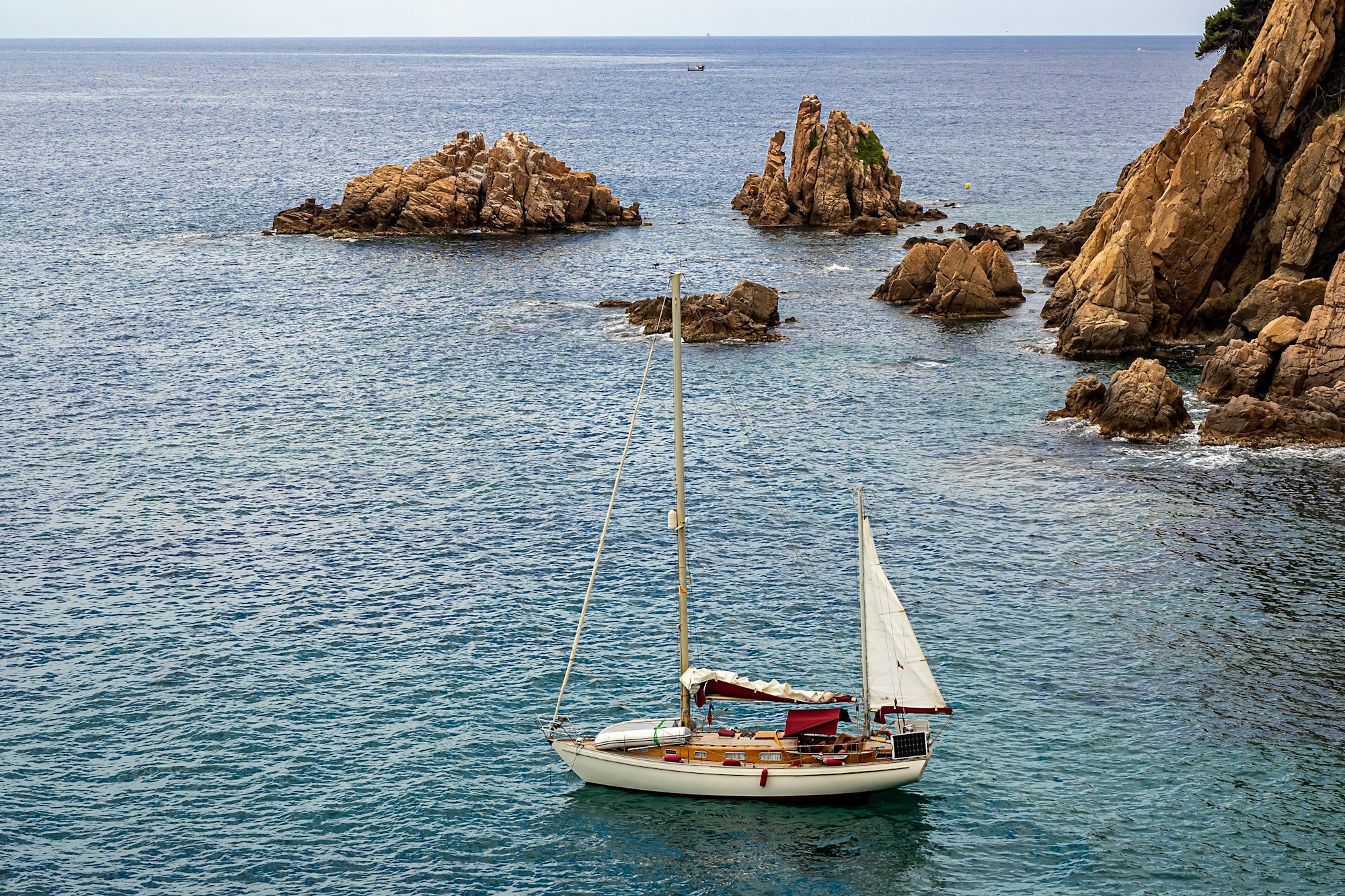 A white sailboat crossing turquoise Mediterranean water beside Mallorca's rocky coast