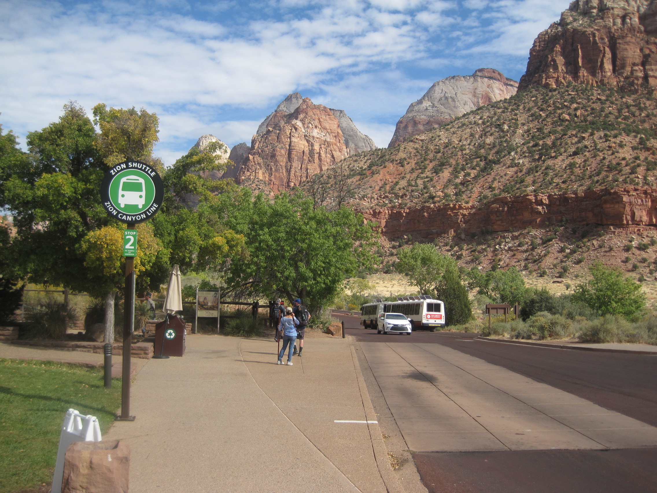 Travelers, shuttle buses, and the Zion Canyon Line sign beneath Zion's towering cliffs
