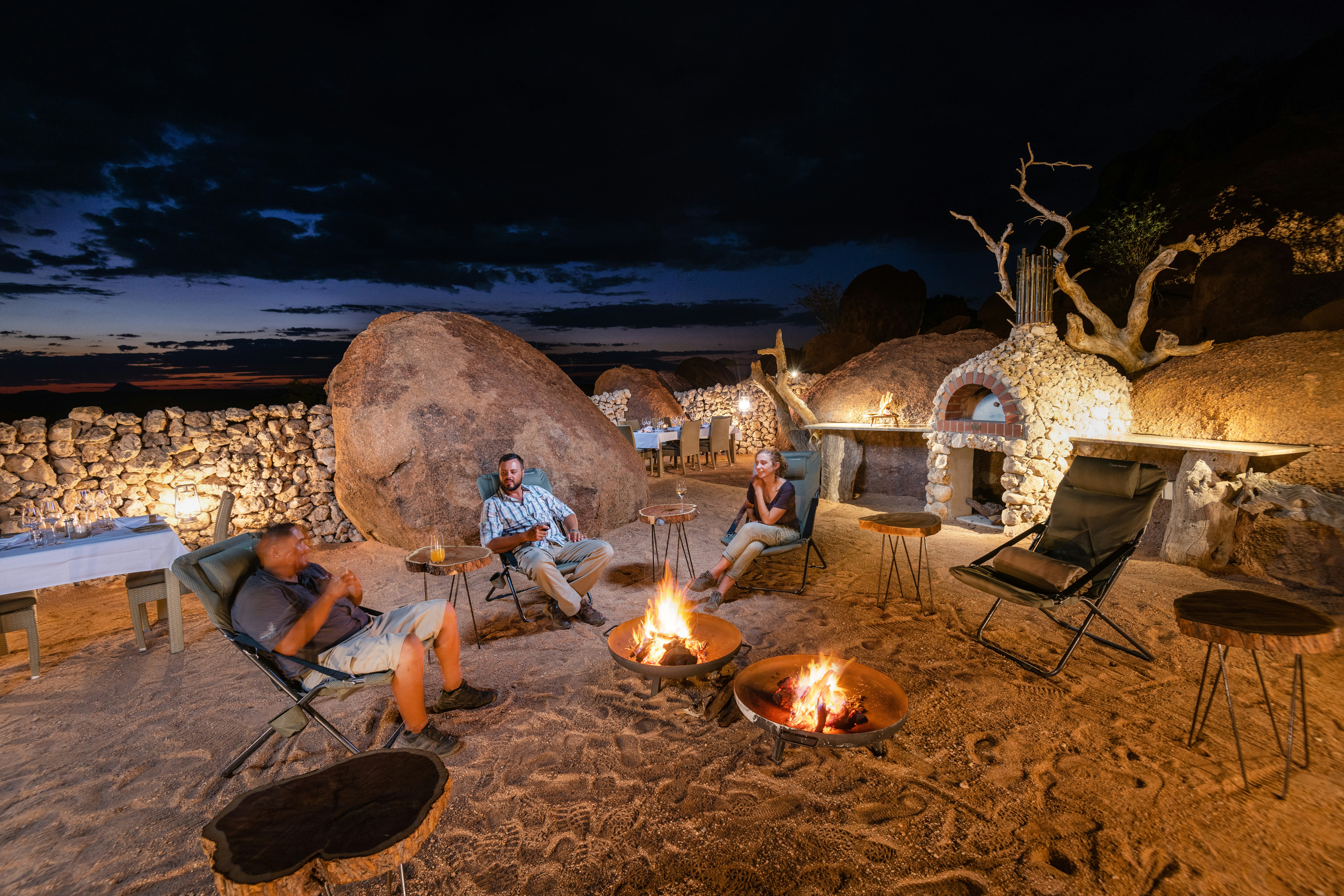 Travelers gathered around a fire at a remote Namibia safari camp beneath the night sky